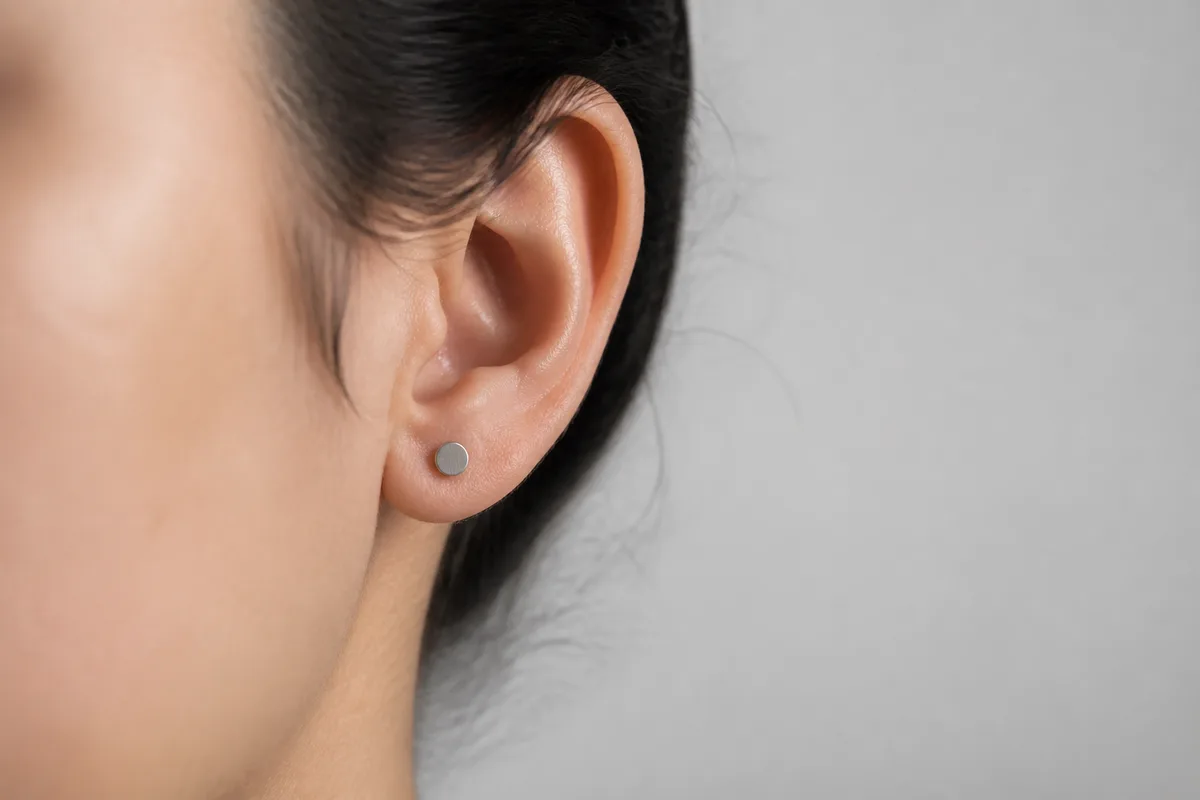 Vue rapprochee d un lobe d oreille portant une tige en titane cicatrisee, arriere-plan neutre et flou
